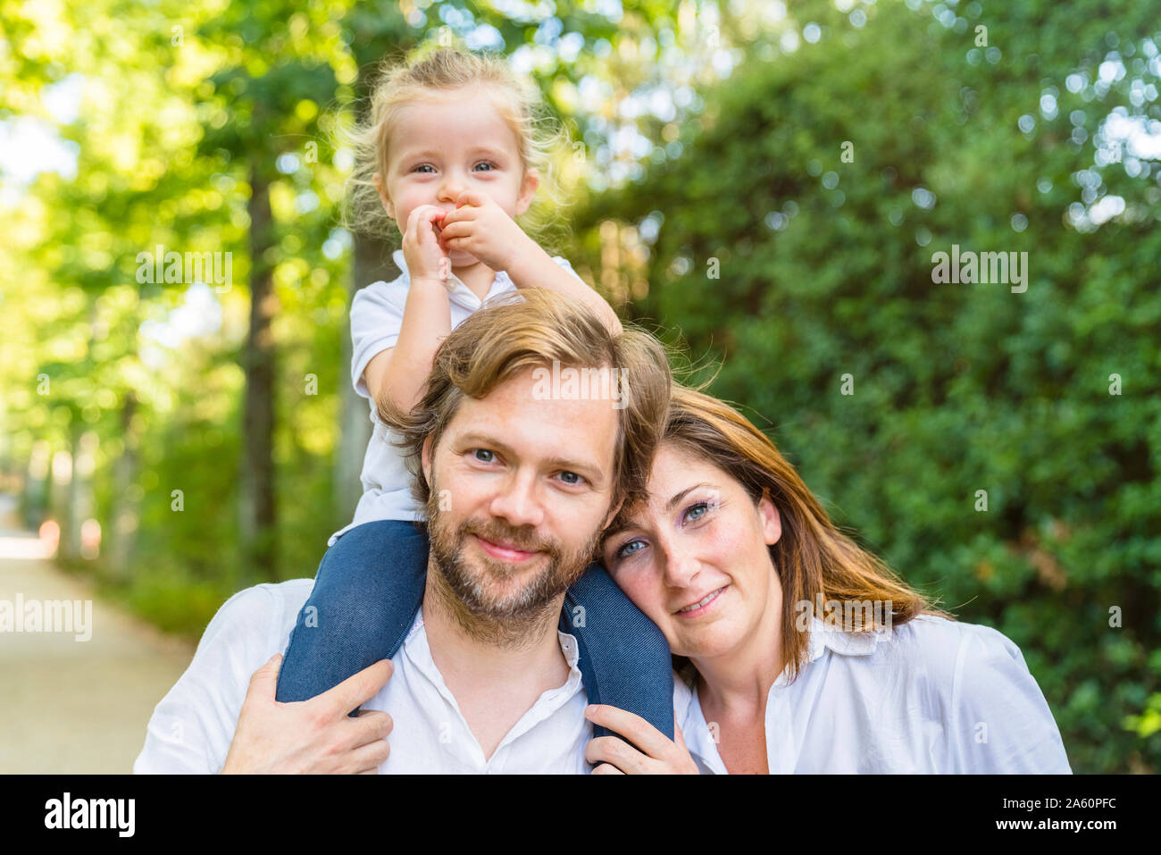 Portait of happy family in a park with father carrying little daughter on his shoulders Stock Photo