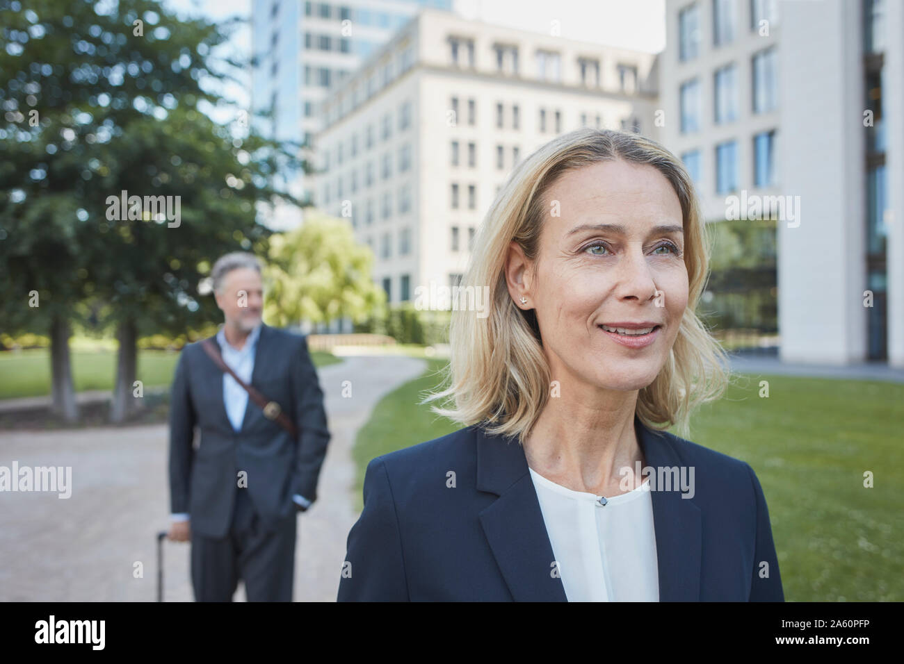 Porrait of smiling blond businesswoman in the city with businessman in background Stock Photo