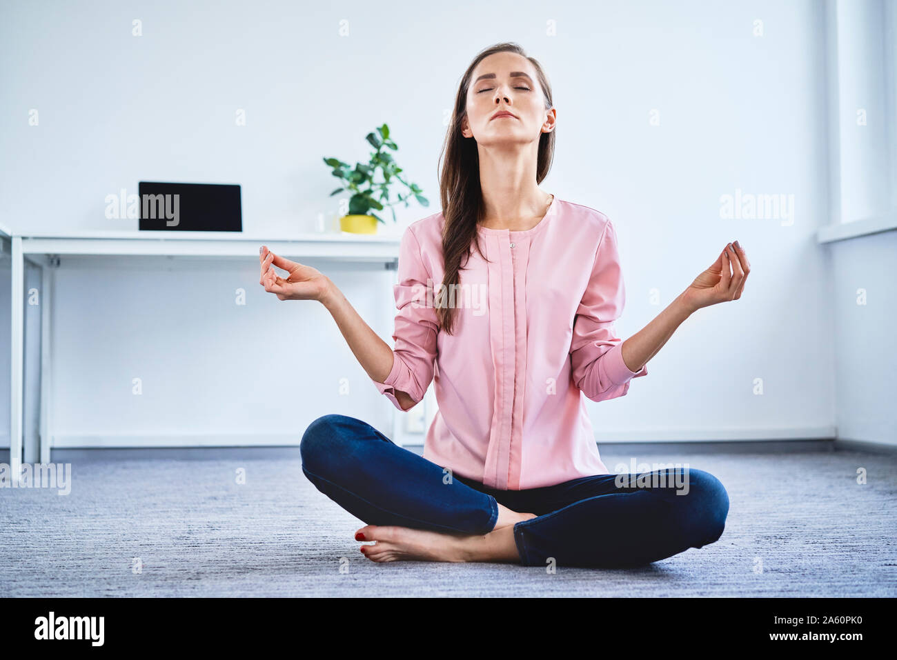 Young woman meditating on floor in office Stock Photo