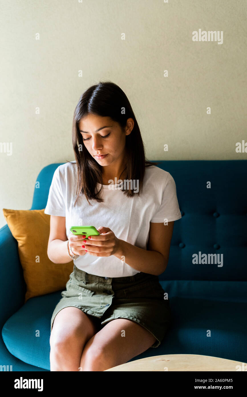 Young woman sitting on a couch using cell phone Stock Photo - Alamy