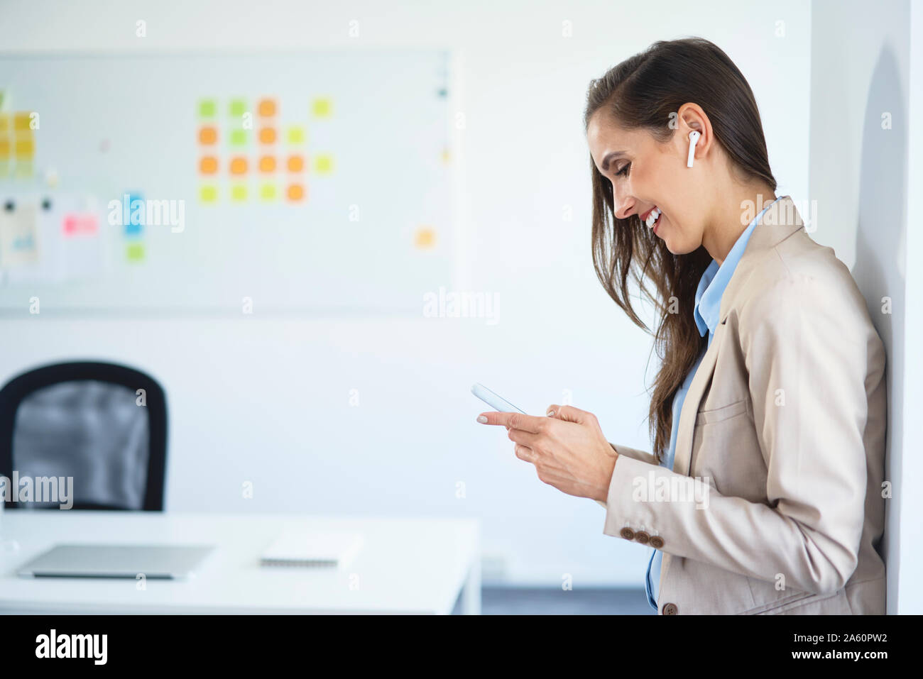 Young businesswoman standing in office using phone and wireless earphones Stock Photo