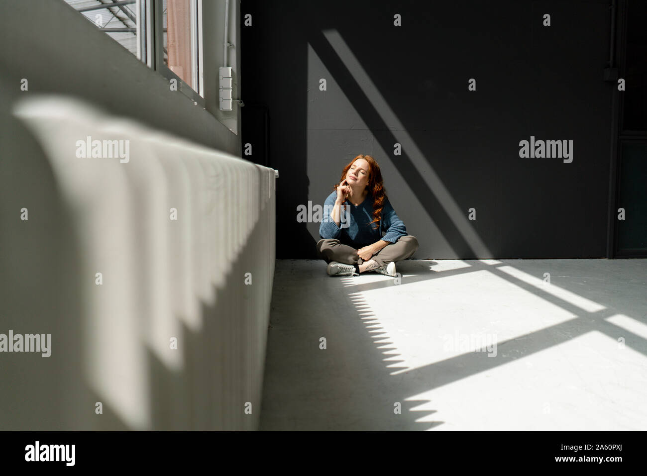 Redheaded woman sitting on floor of a loft enjoying sunlight Stock Photo