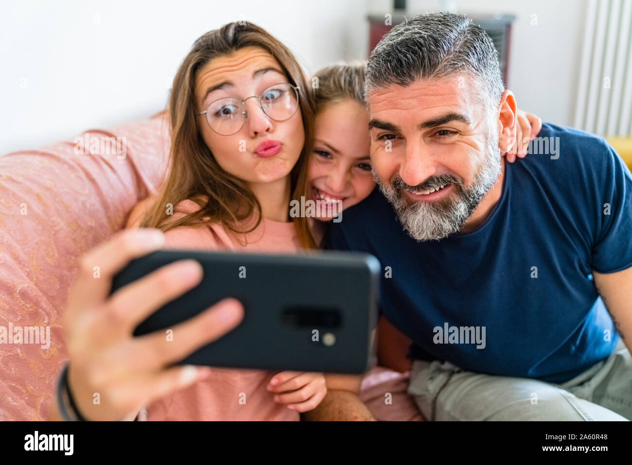 Happy father with two daughters taking selfie on couch at home Stock Photo