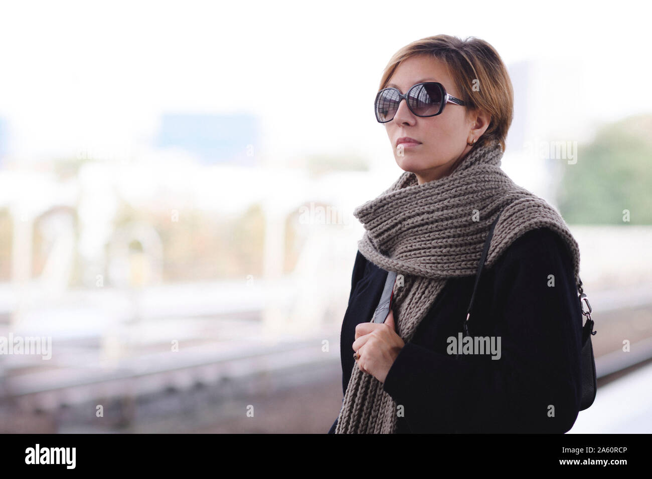 Mature woman with sunglasses wearing black coat and wool scarf waiting at platform Stock Photo