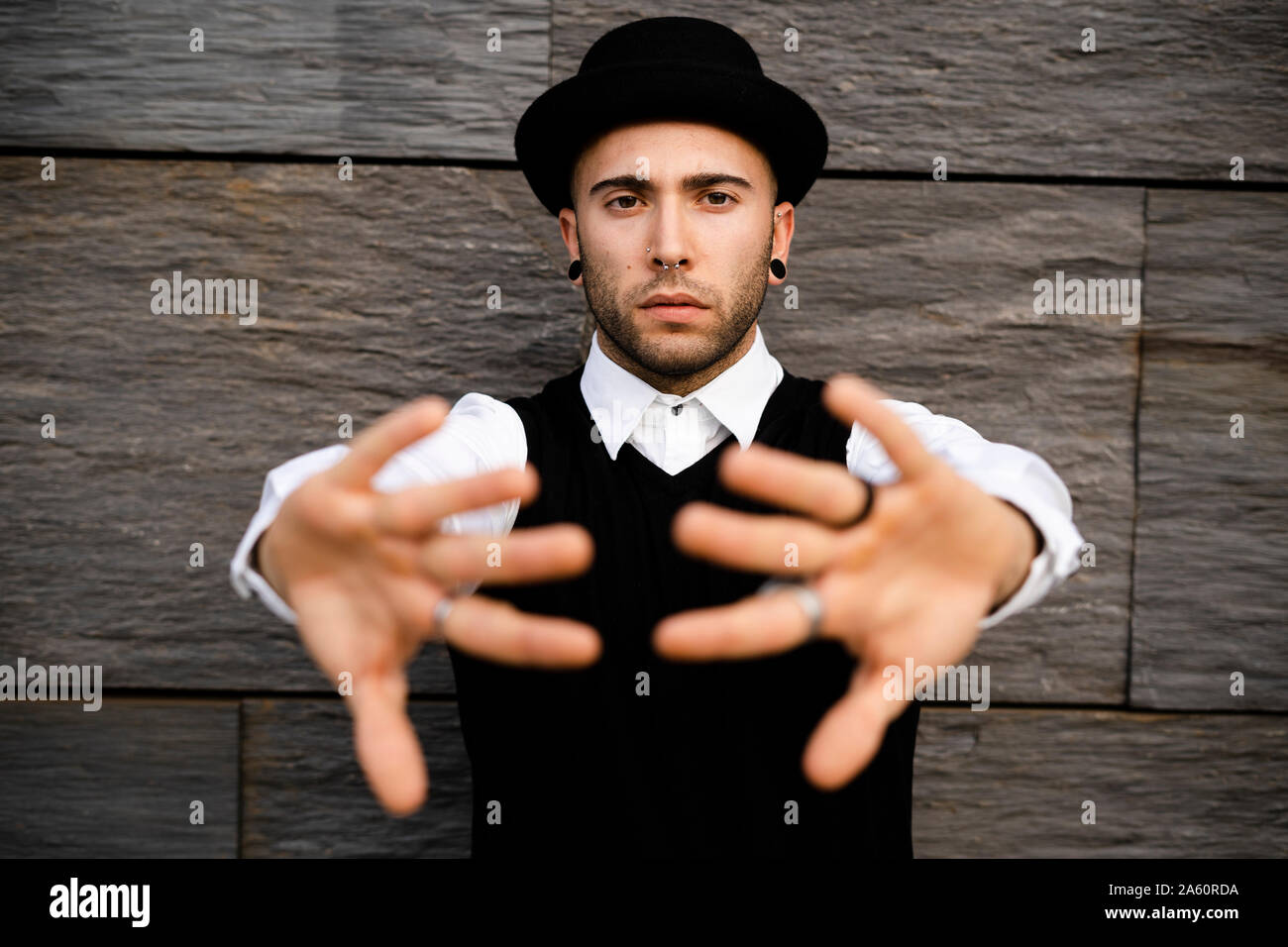 Portrait of serious young man with nose piercing and earrings raising hands Stock Photo