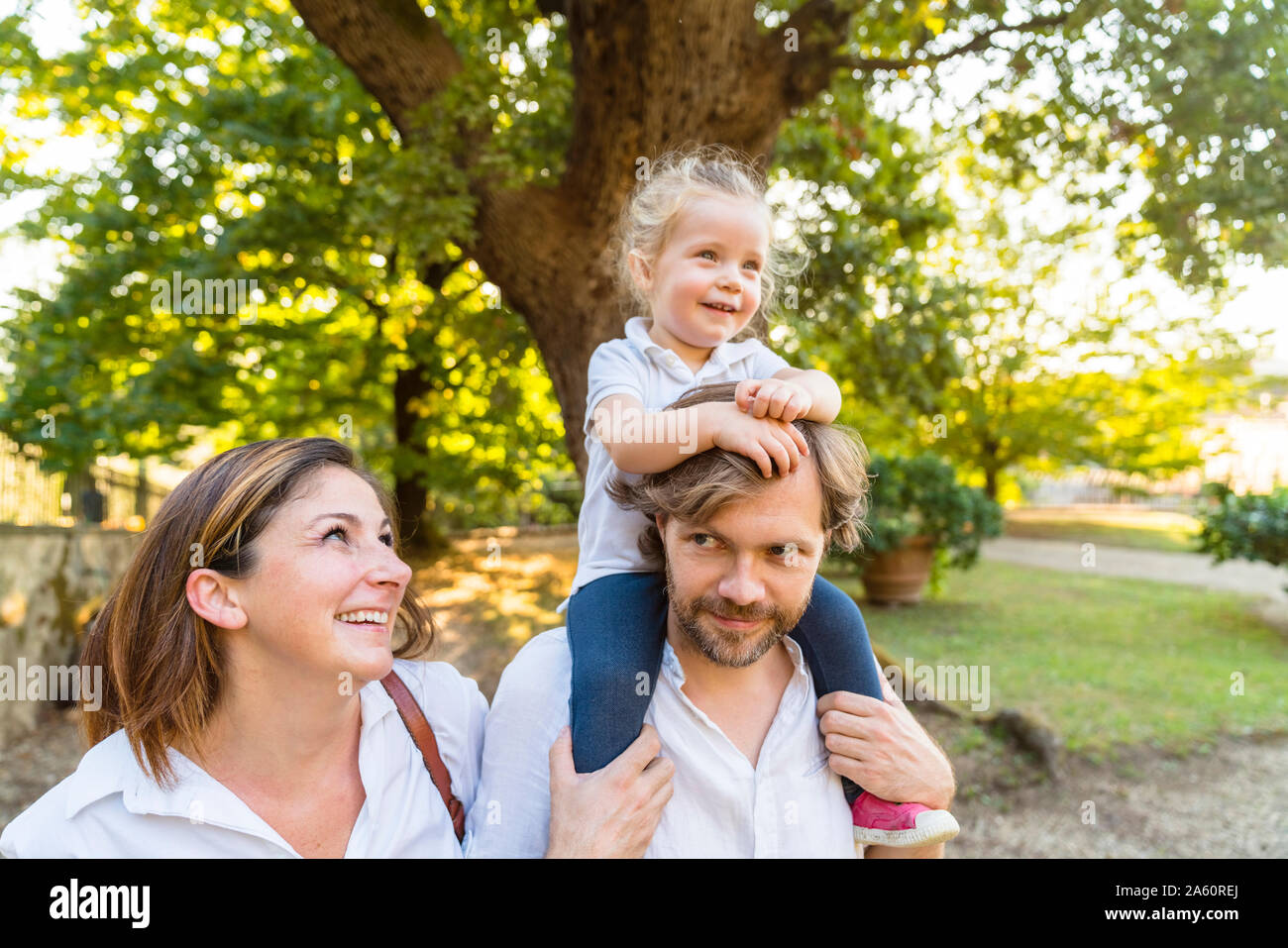 Happy family in a park with father carrying little daughter on his shoulders Stock Photo