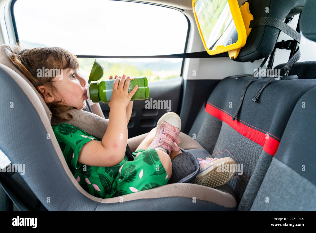 Toddler girl sitting on a car seat with a mirror drinking water Stock Photo