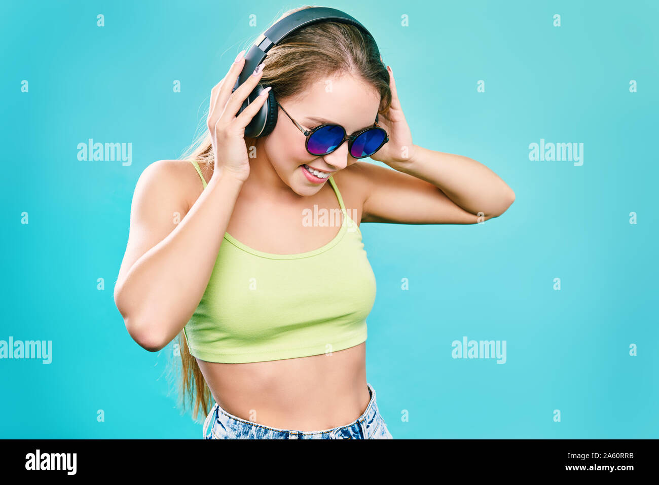 Pretty cool girl having fun and listens to music in the headphones on smartphone over colorful background. Stock Photo