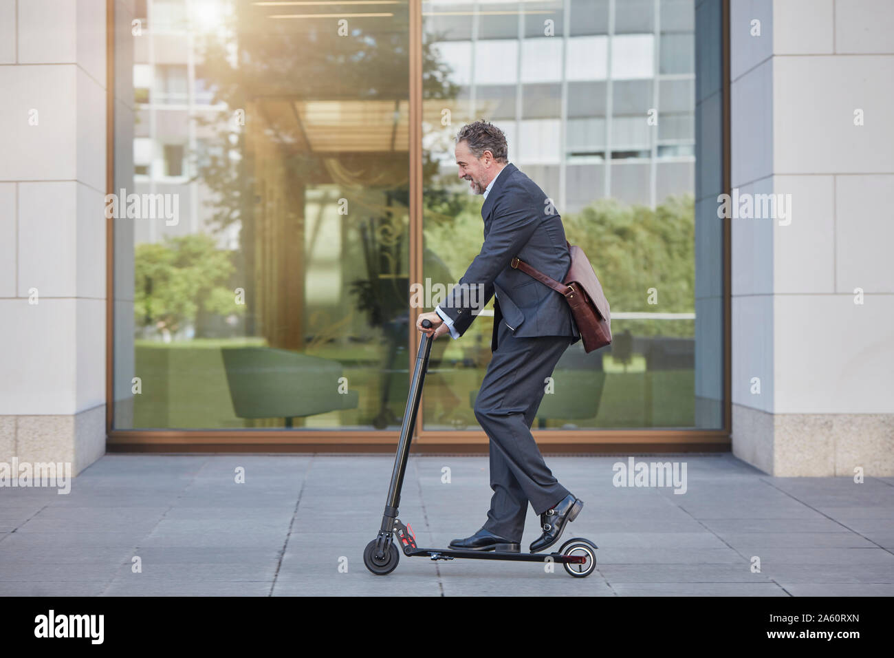 Businessman on e-scooter passing office building in the city Stock Photo