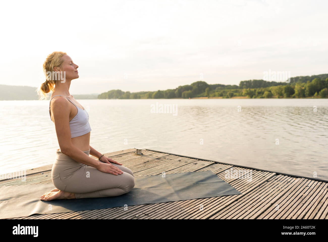 Young woman practicing yoga on a jetty at a lake Stock Photo