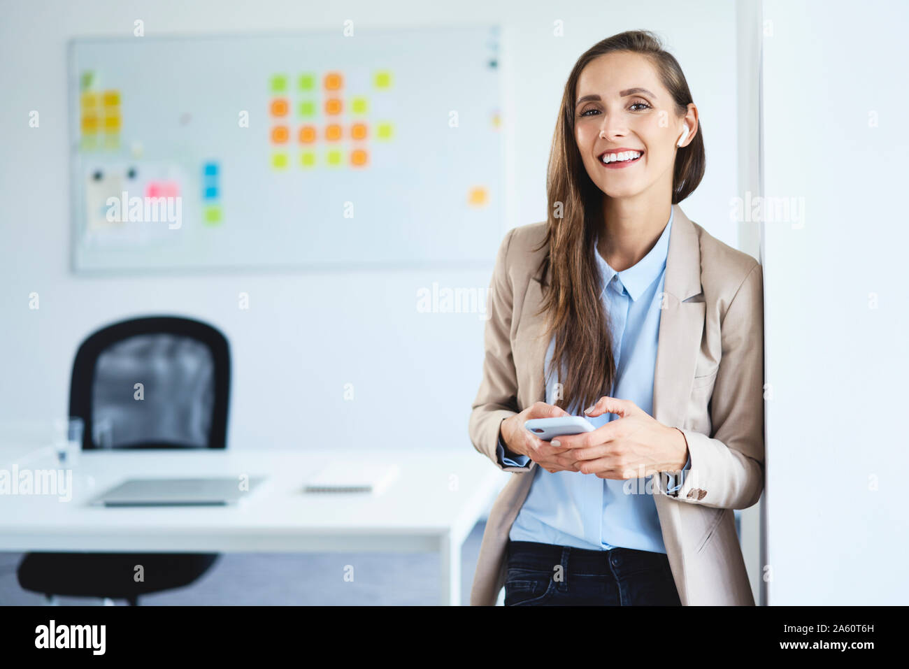 Young businesswoman standing in office holding phone and smiling at camera Stock Photo