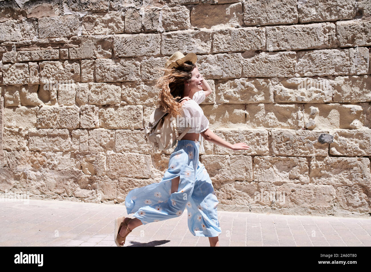 Happy young woman running along a wall Stock Photo