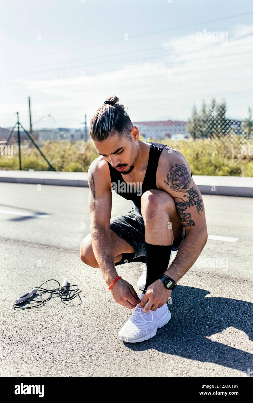 Sporty young man tying shoes before training on a road Stock Photo