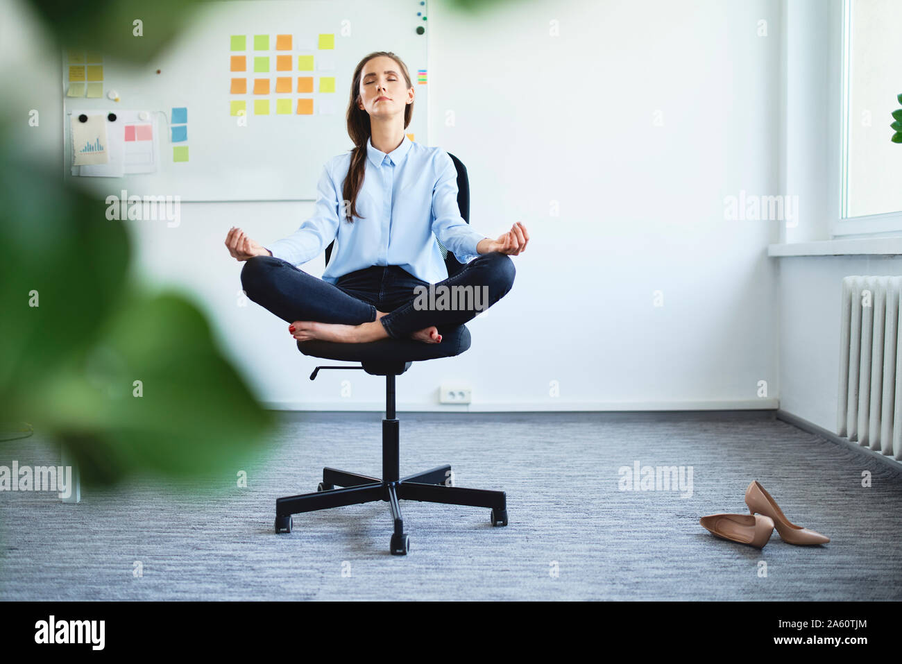 Serene young woman meditating while sitting on office chair Stock Photo ...
