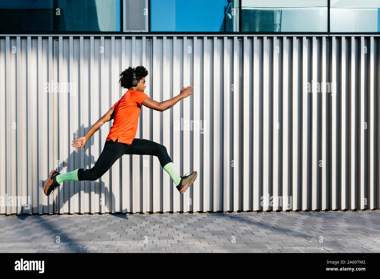 Young man jumping in the city, metallic wall in the background Stock Photo