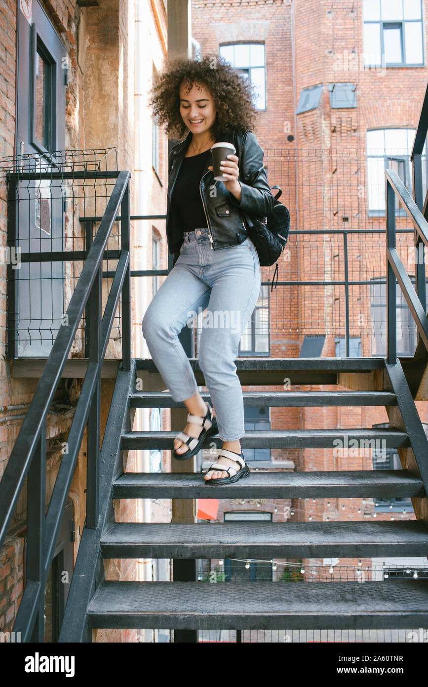 Portrait of smiling teenage girl with coffee to go walking downstairs Stock Photo