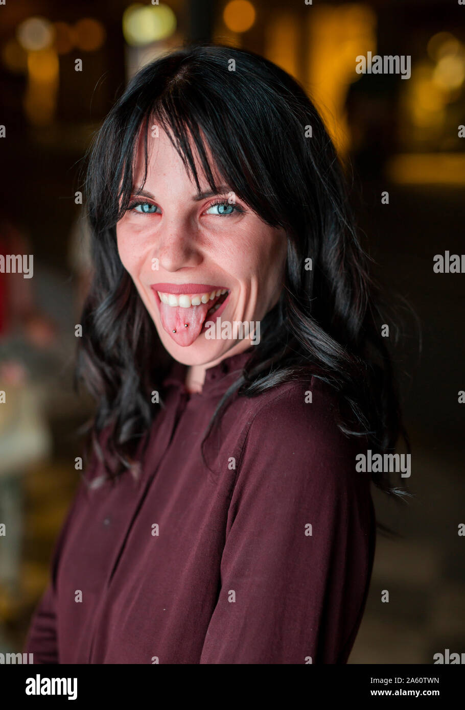 Portrait of a young woman in the city sticking out tongue at night Stock Photo