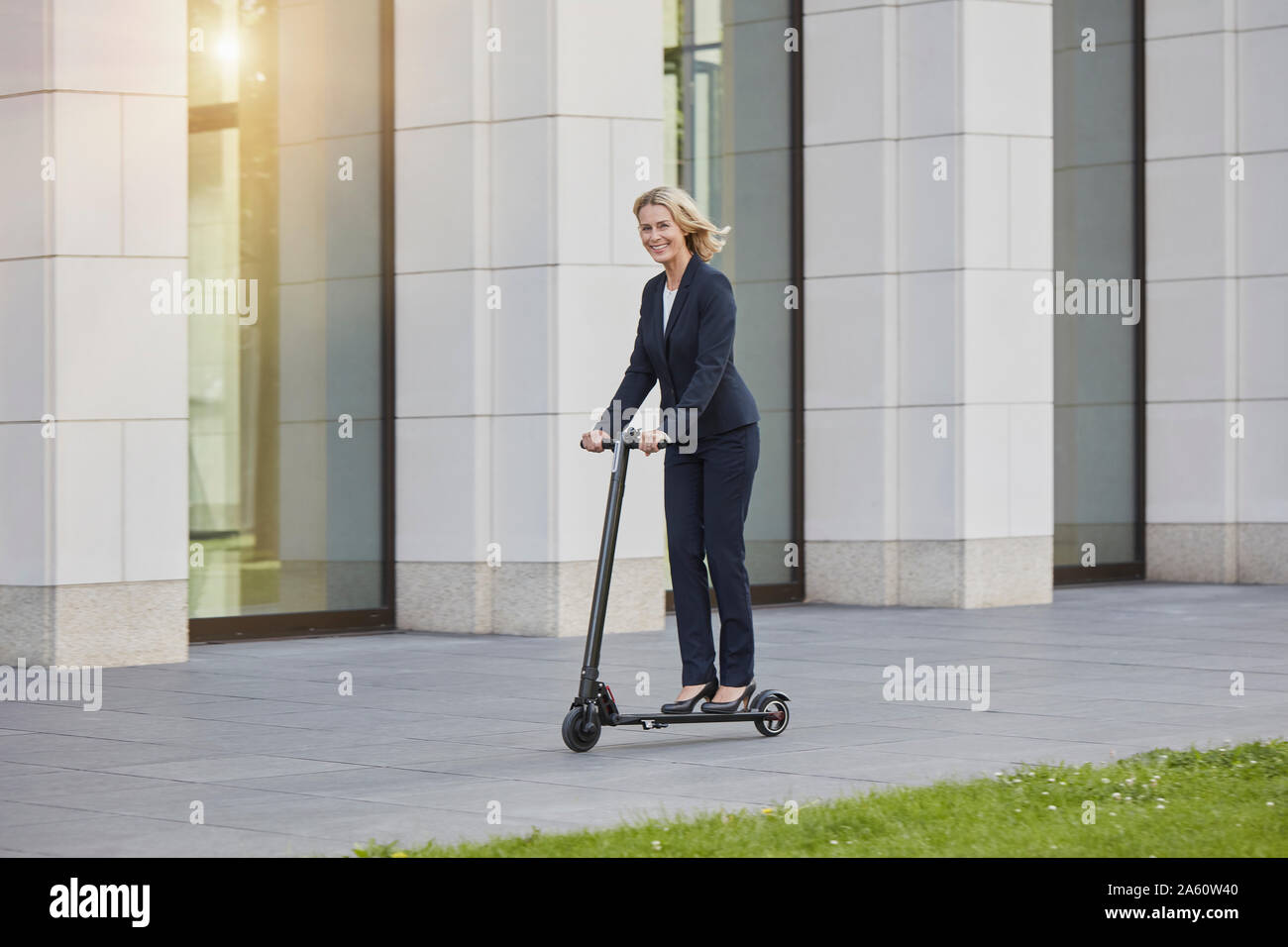 Businesswoman on e-scooter passing office building in the city Stock Photo