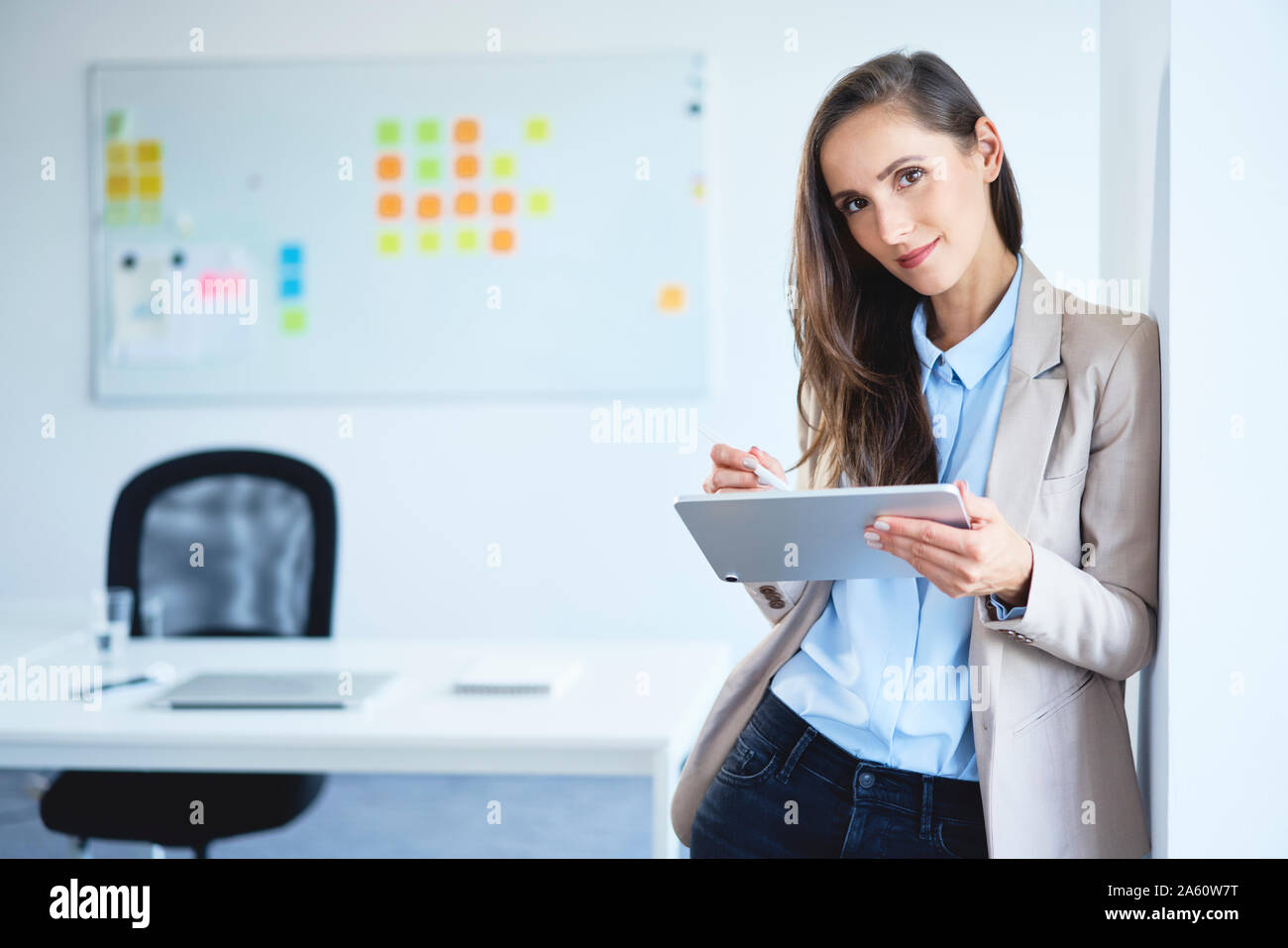 Young businesswoman smiling at camera while using tablet in office Stock Photo