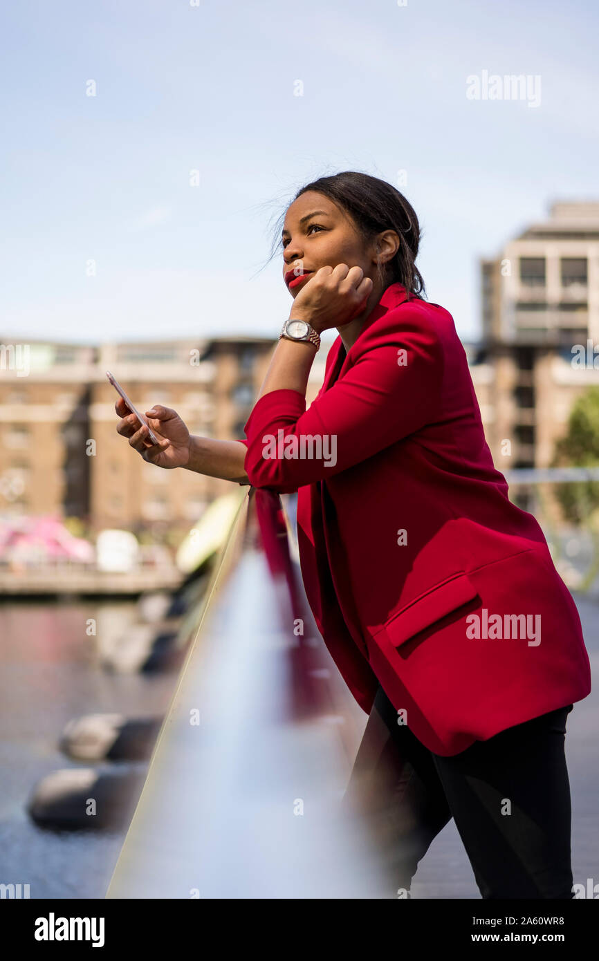 Portrait of pensive businesswoman leaning on bridge railing looking up, London, UK Stock Photo