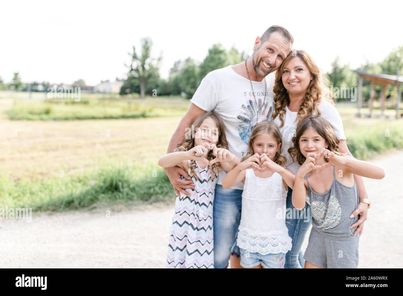 Happy parents with three triplet sisters shaping a heart outdoors Stock Photo