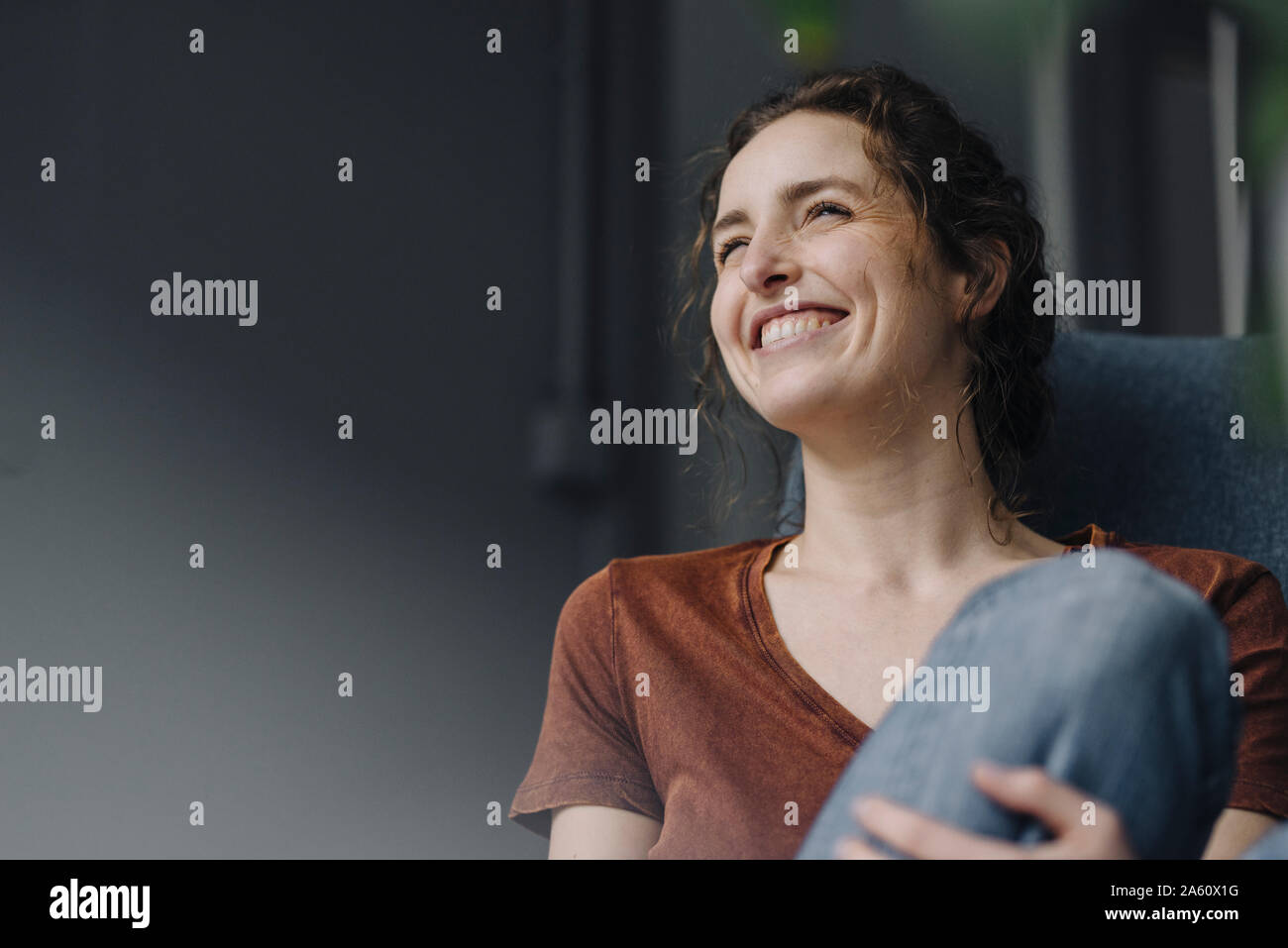 Portrait of laughing young woman sitting on lounge chair at home Stock ...