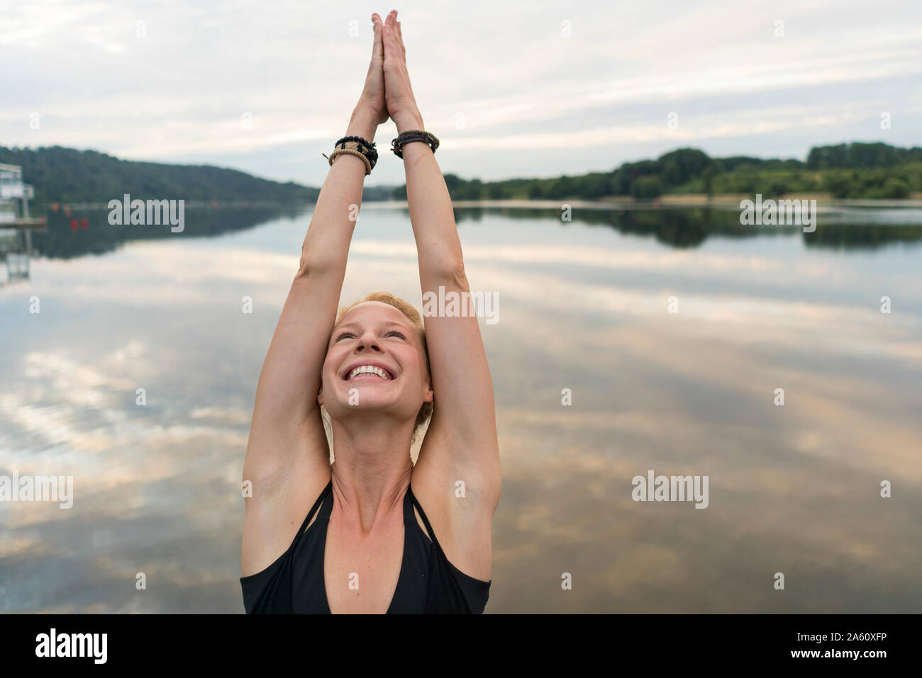 Happy young woman raising her arms at a lake Stock Photo