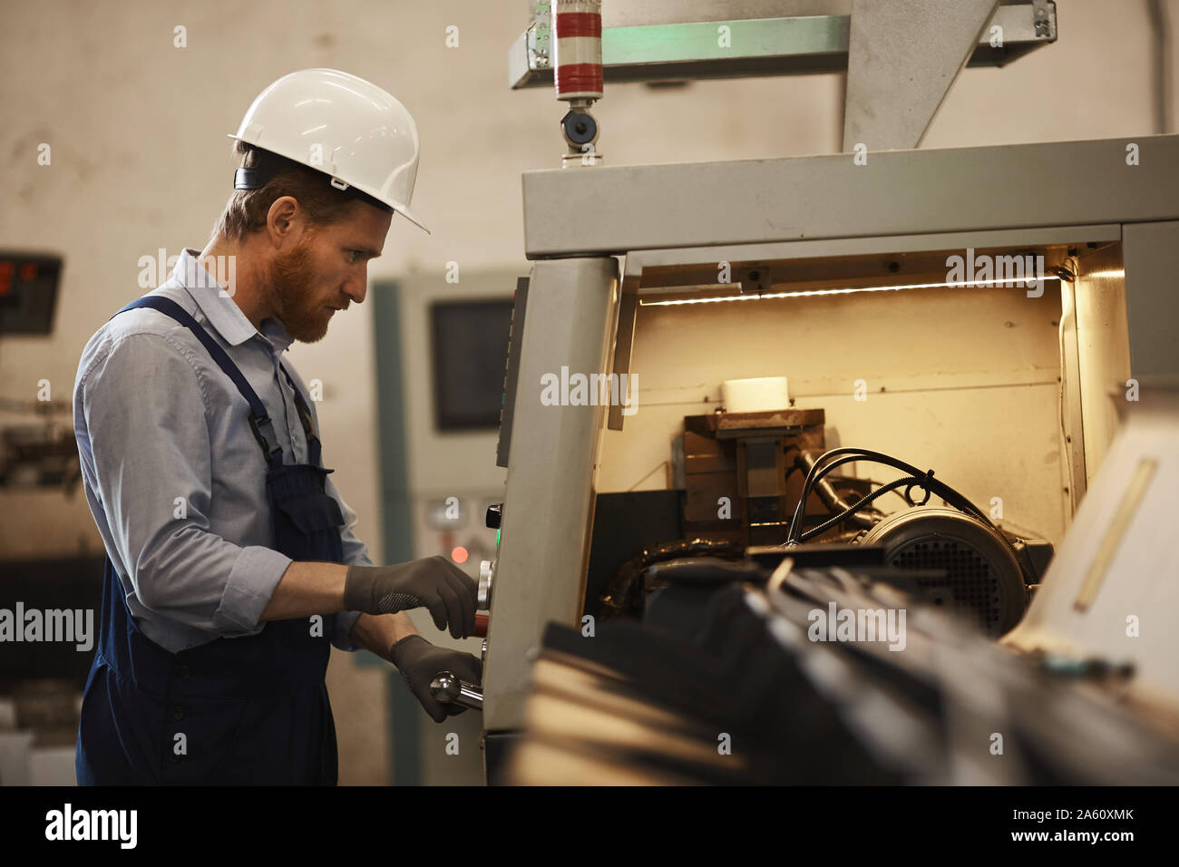 Young serious worker in protective work wear standing and controlling the machine in the factory Stock Photo