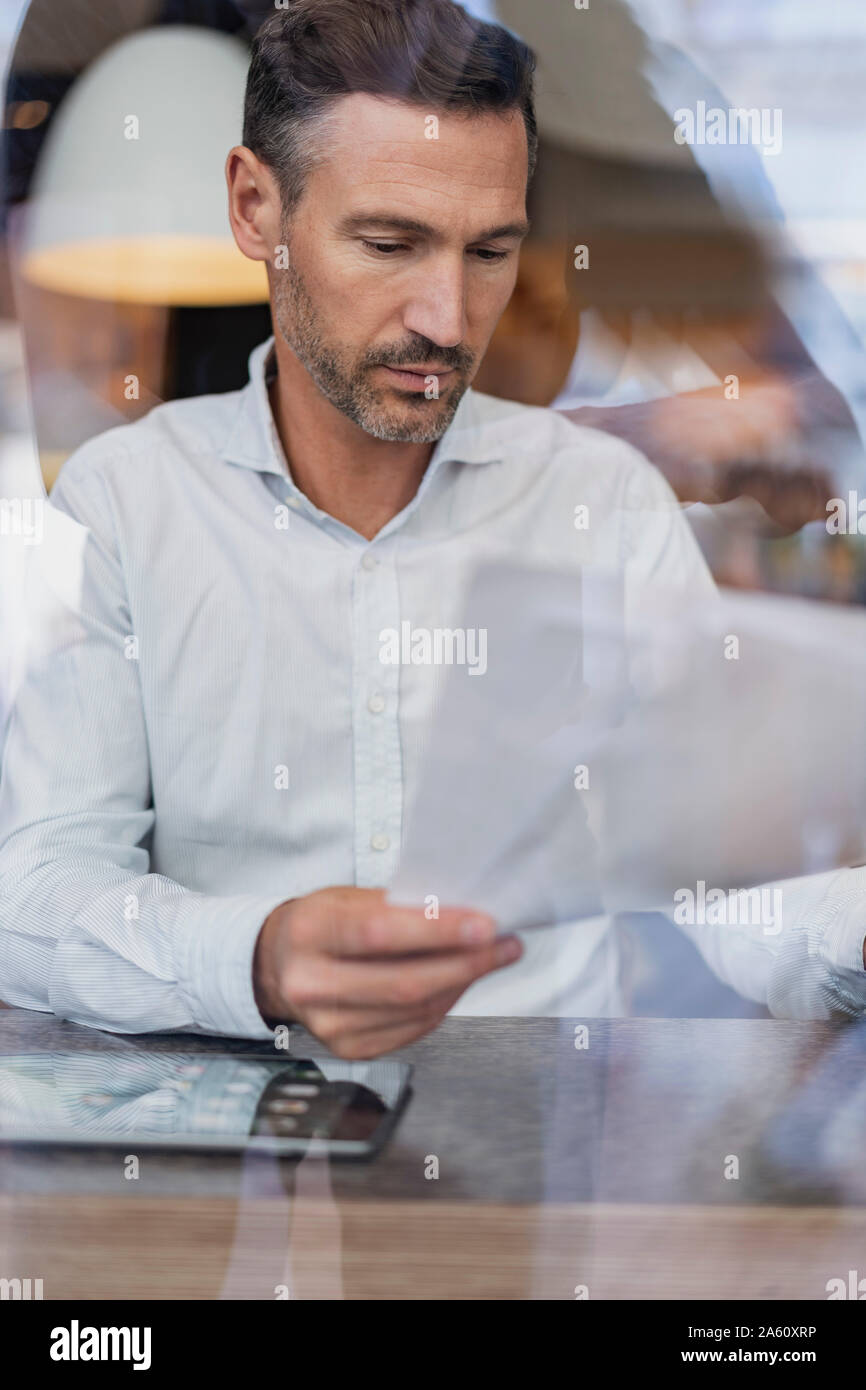 Businessman behind windowpane in a cafe reading papers Stock Photo