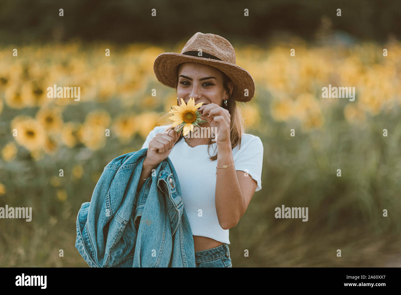 Portrait of young woman with blue denim jacket and hat in a field of sunflowers Stock Photo