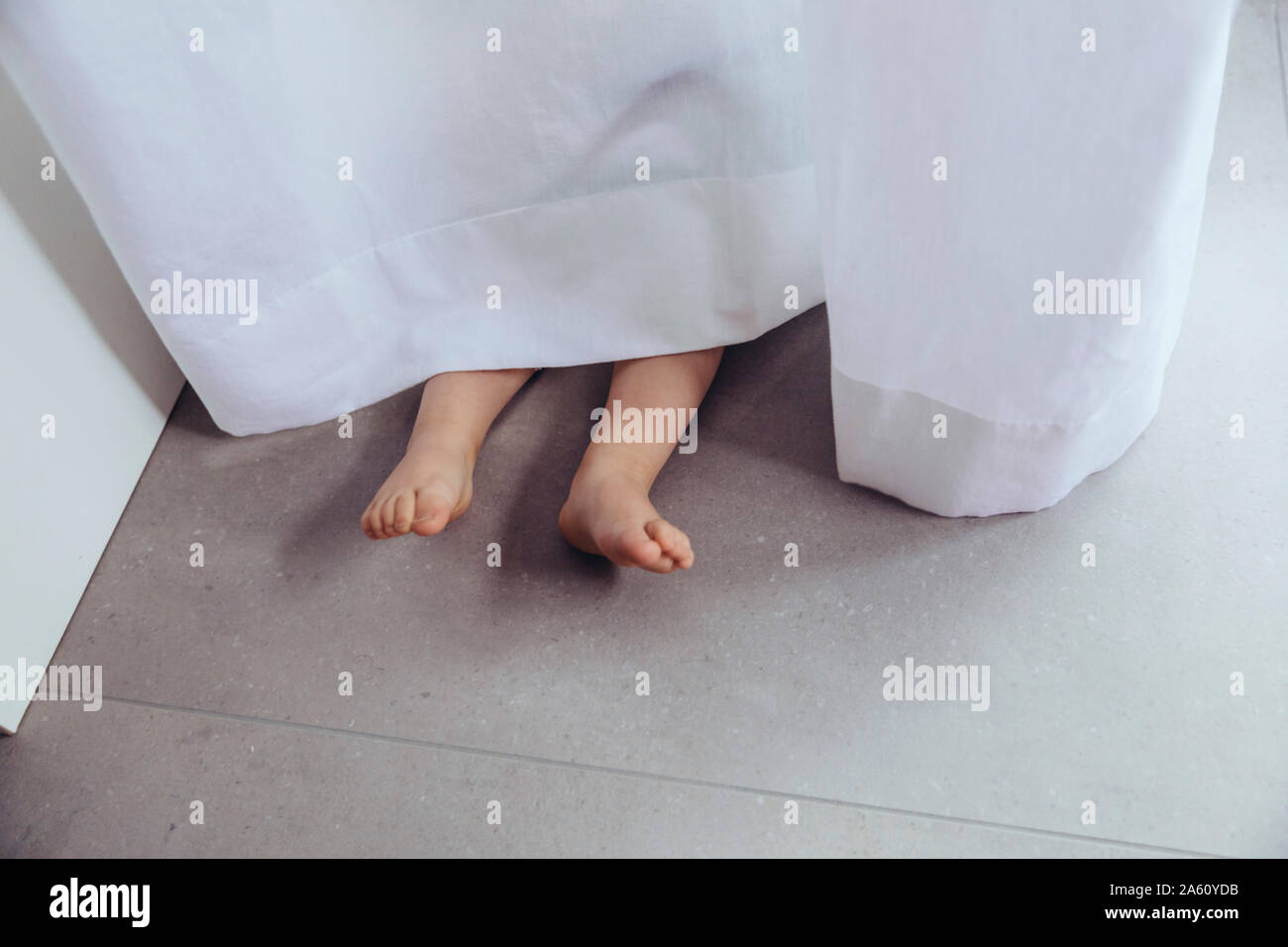 Legs and feet of little boy, hiding behind curtain Stock Photo