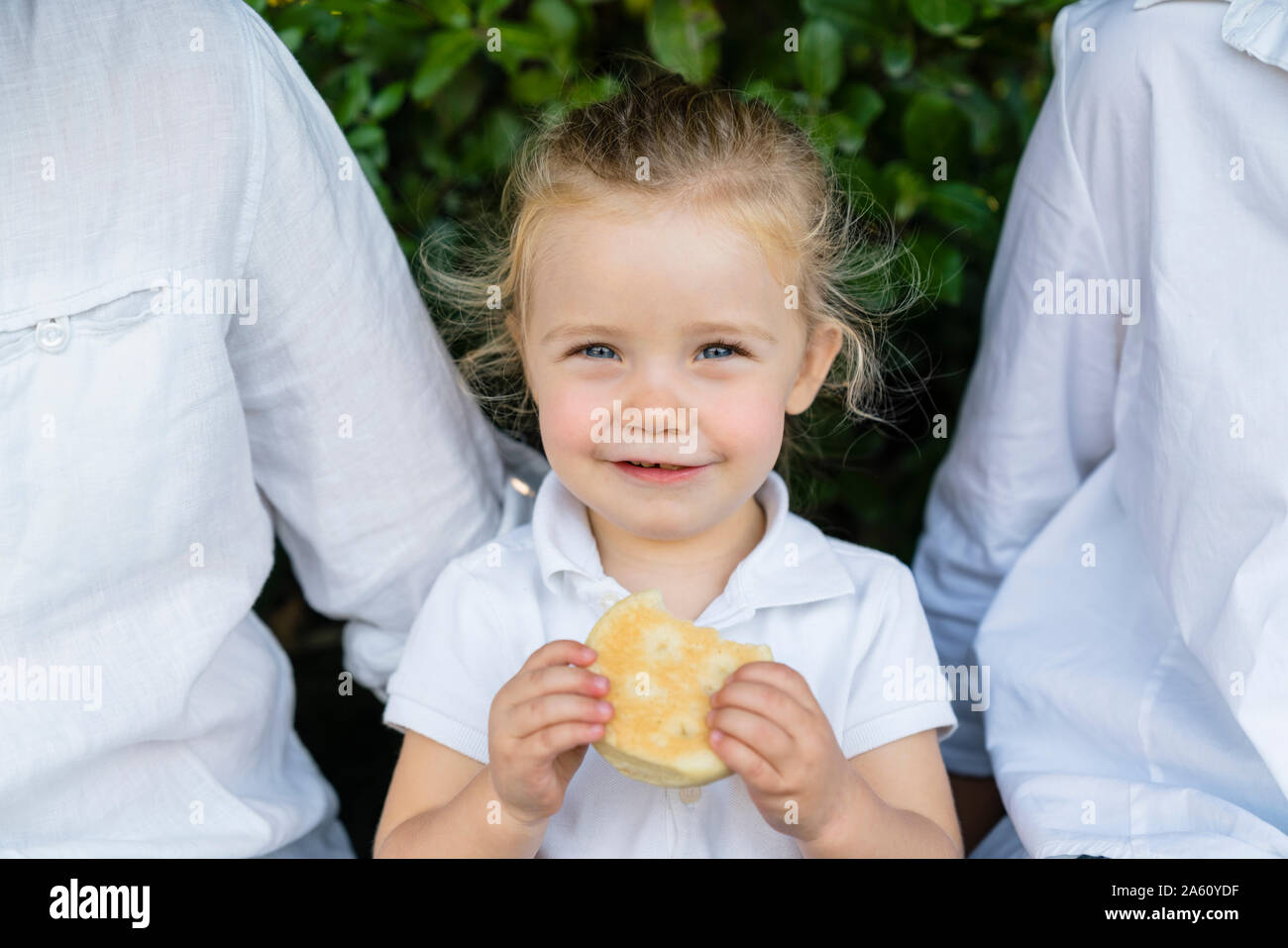 Portrait of little girl with a snack sitting amidst parents Stock Photo