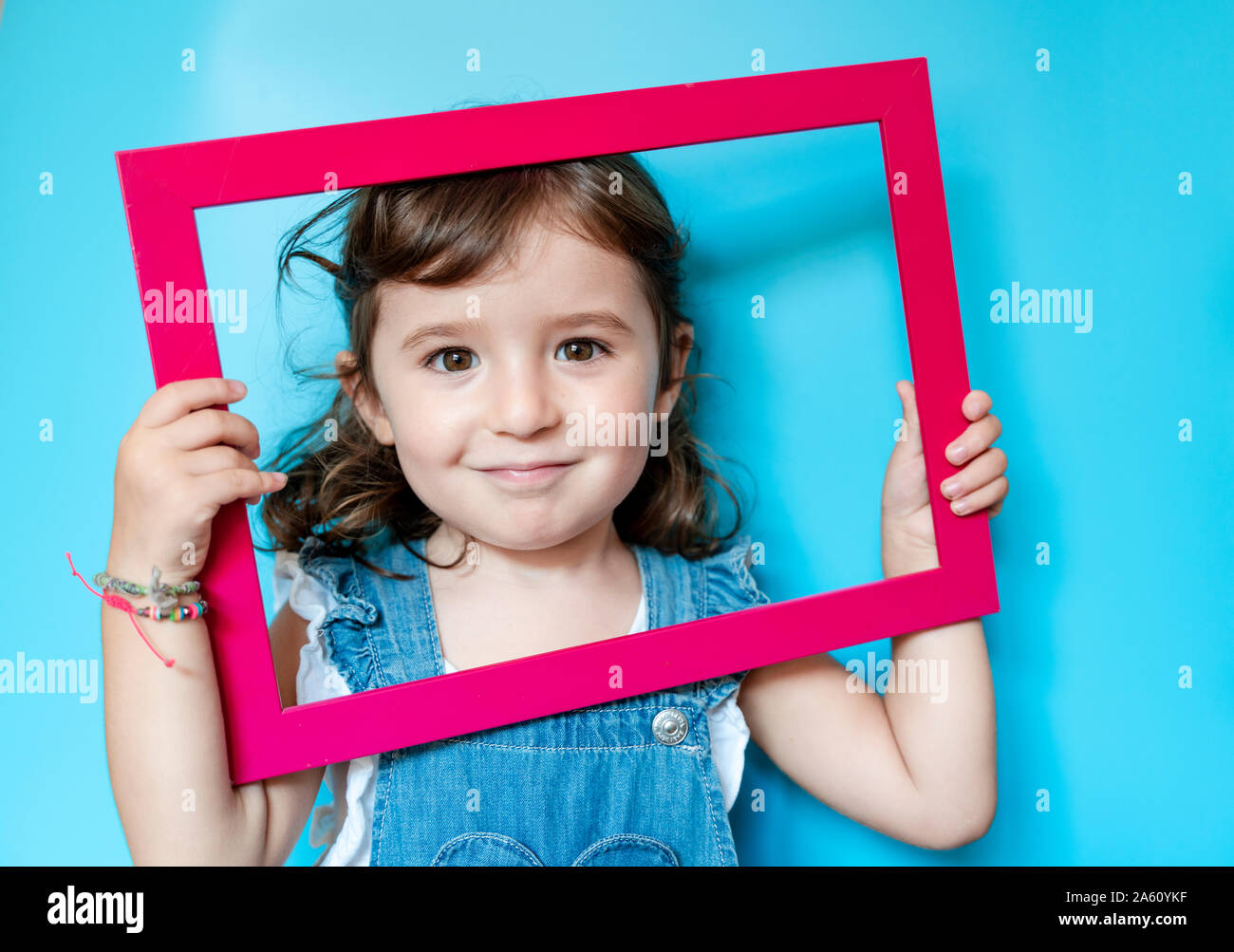 Portrait of cute little girl holding a picture frame on blue background Stock Photo