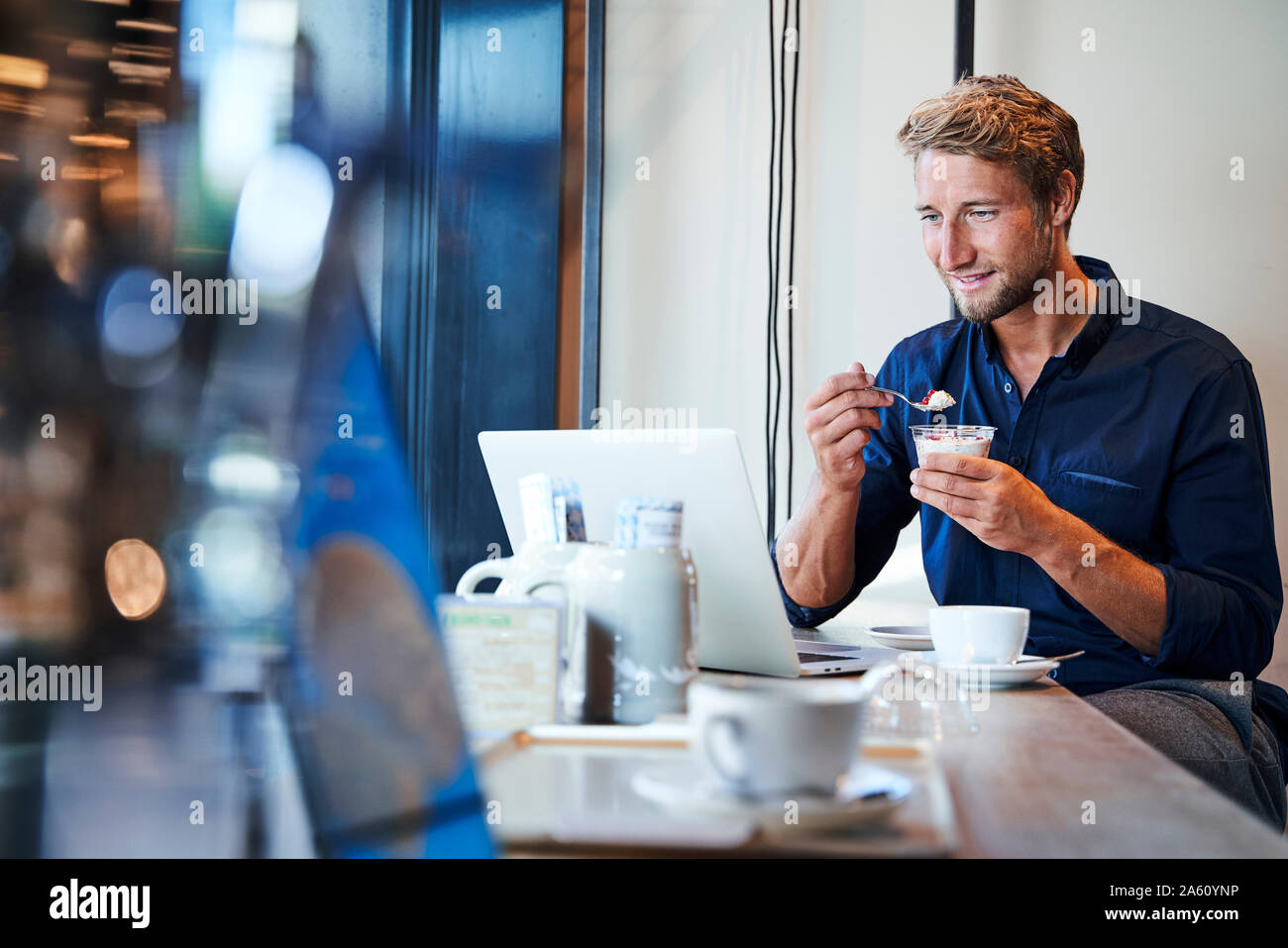 Young businessman eating and using laptop in a cafe Stock Photo