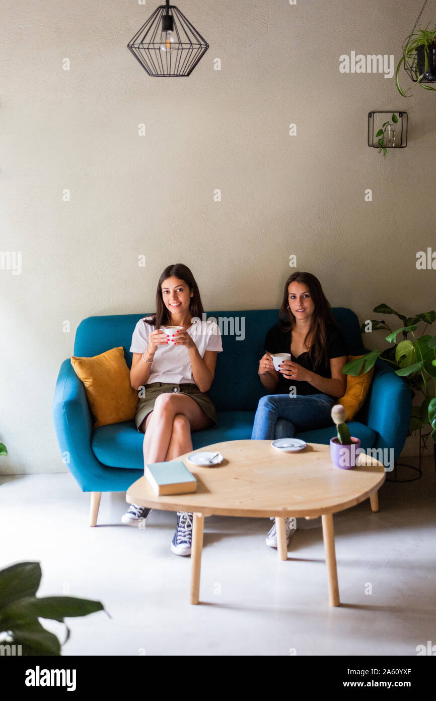 Two young female friends sitting on a couch in a cafe Stock Photo