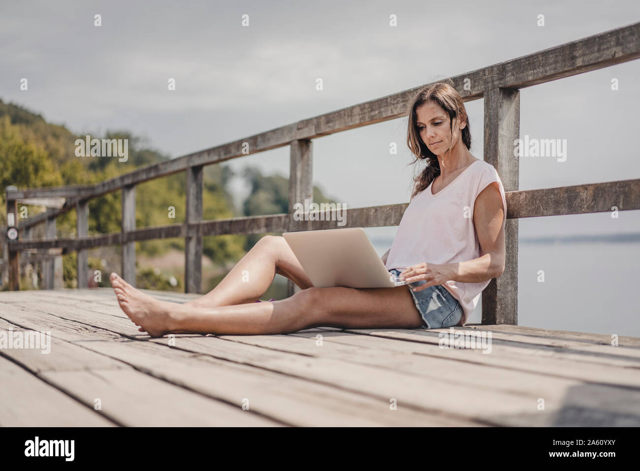 Woman sitting on wood bridge, using laptop Stock Photo