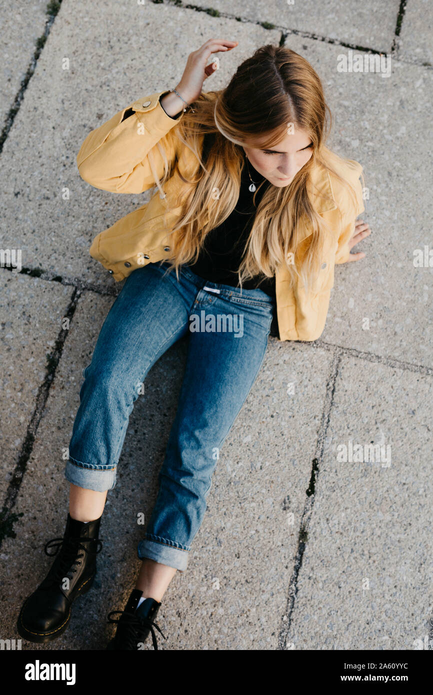 Young woman wearing yellow jacket sitting on the ground Stock Photo - Alamy