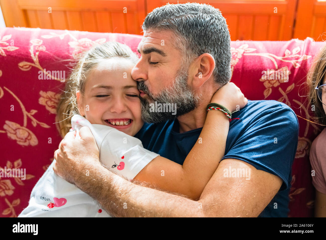 Father hugging with daughter on couch at home Stock Photo