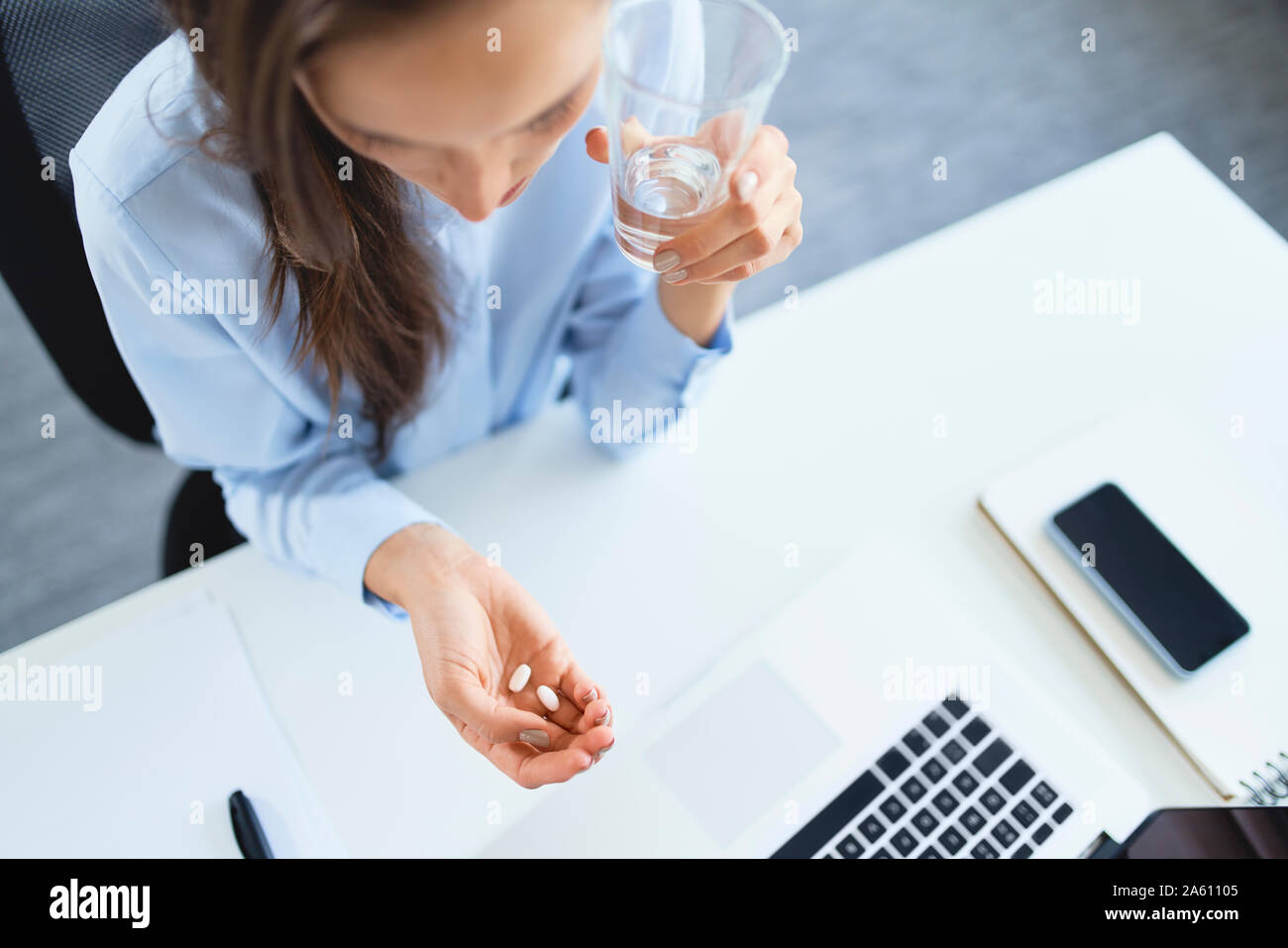 Overhead view of woman taking painkillers while sitting on office Stock Photo