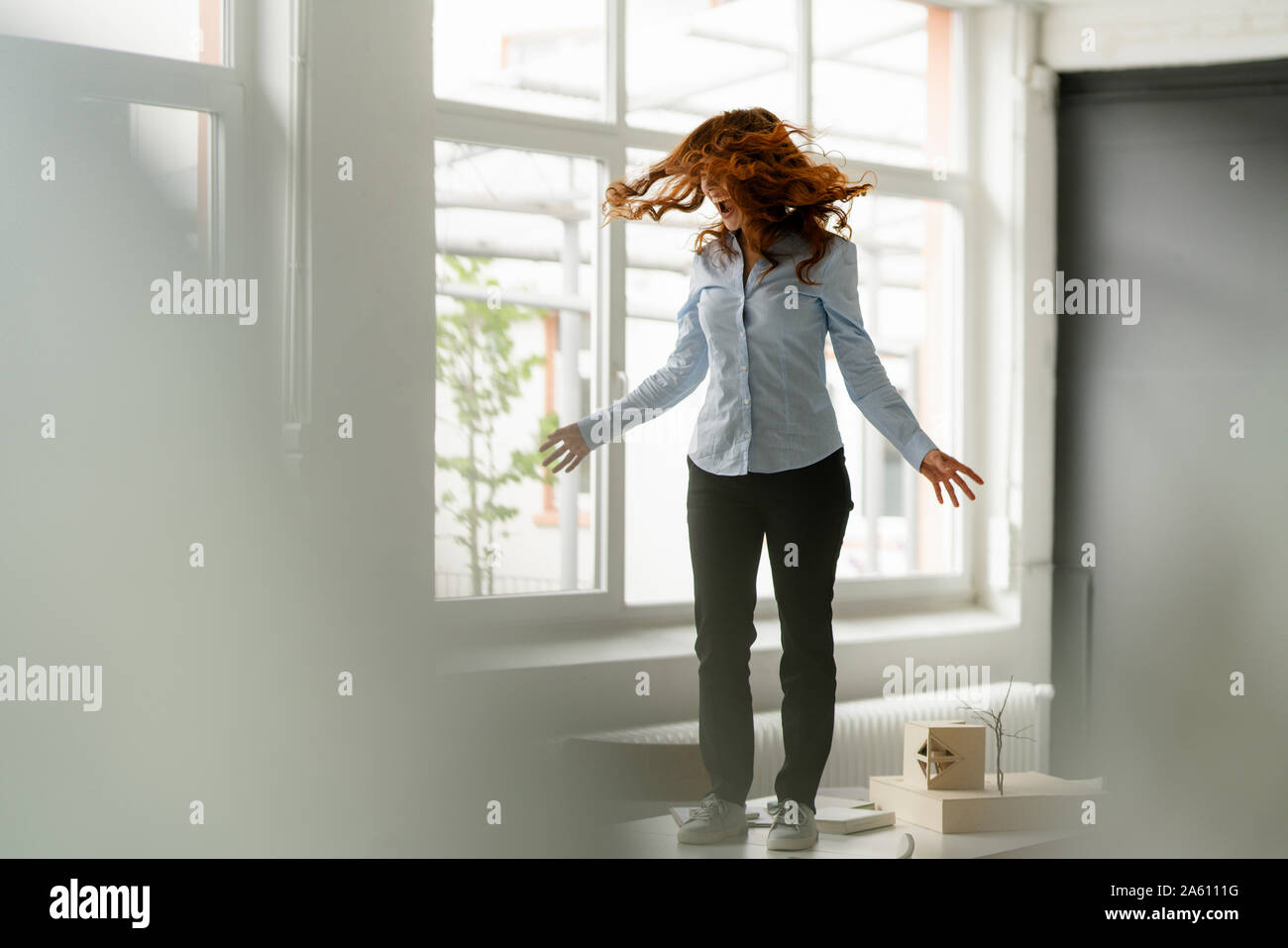 Redheaded woman standing on desk in a loft moving and screaming Stock Photo