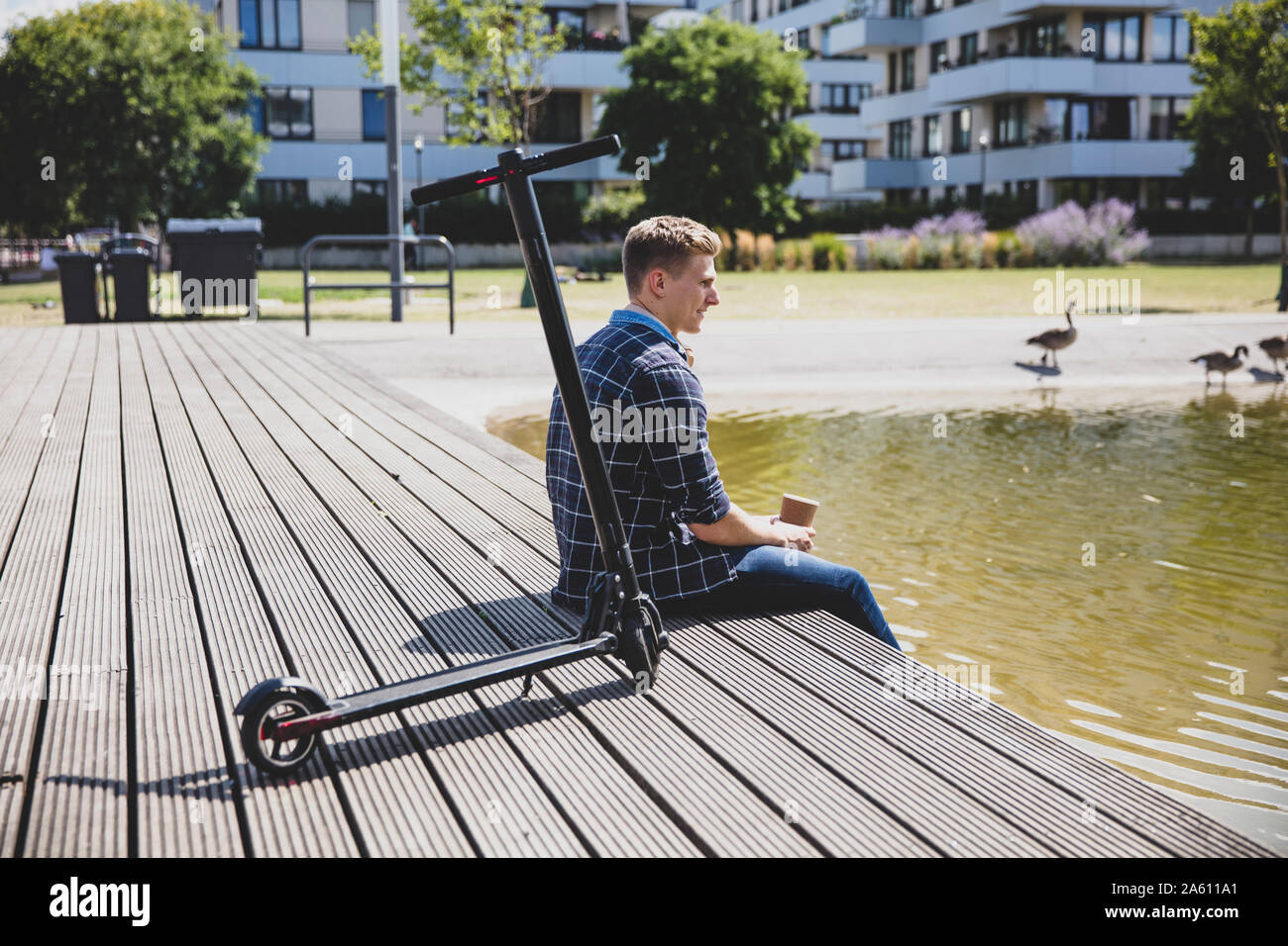 Young man with e-scooter sitting on boardwalk Stock Photo