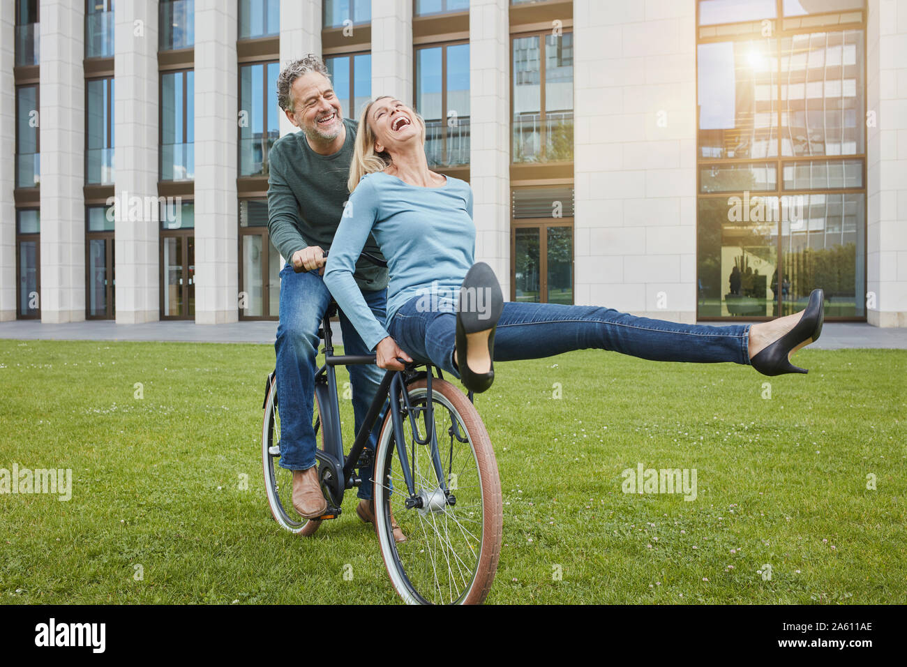 Exuberant mature couple riding bicycle on lawn in the city Stock Photo