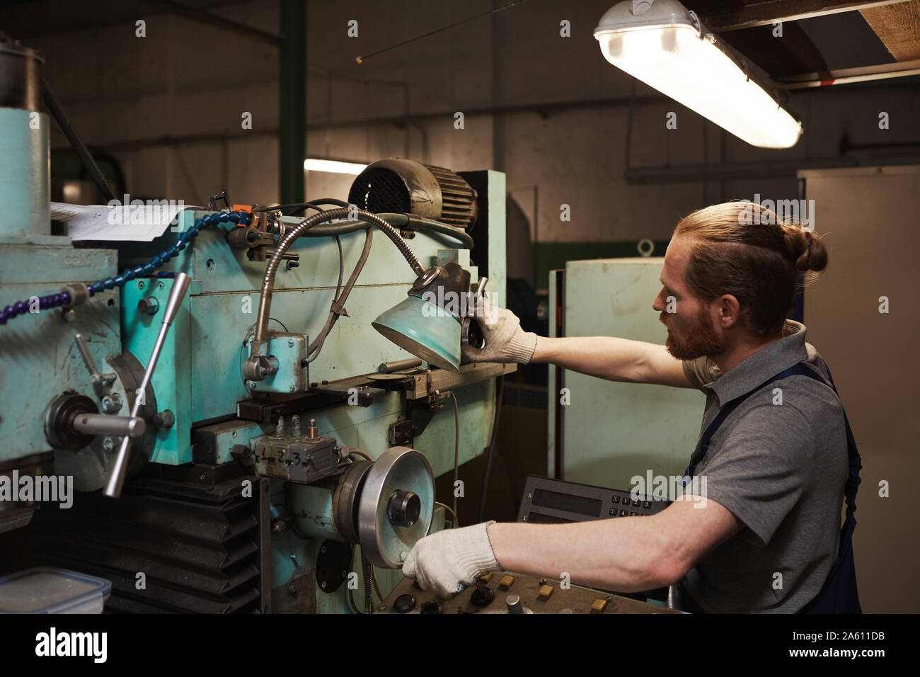 Young mechanic in work wear standing near the lathe and working on it