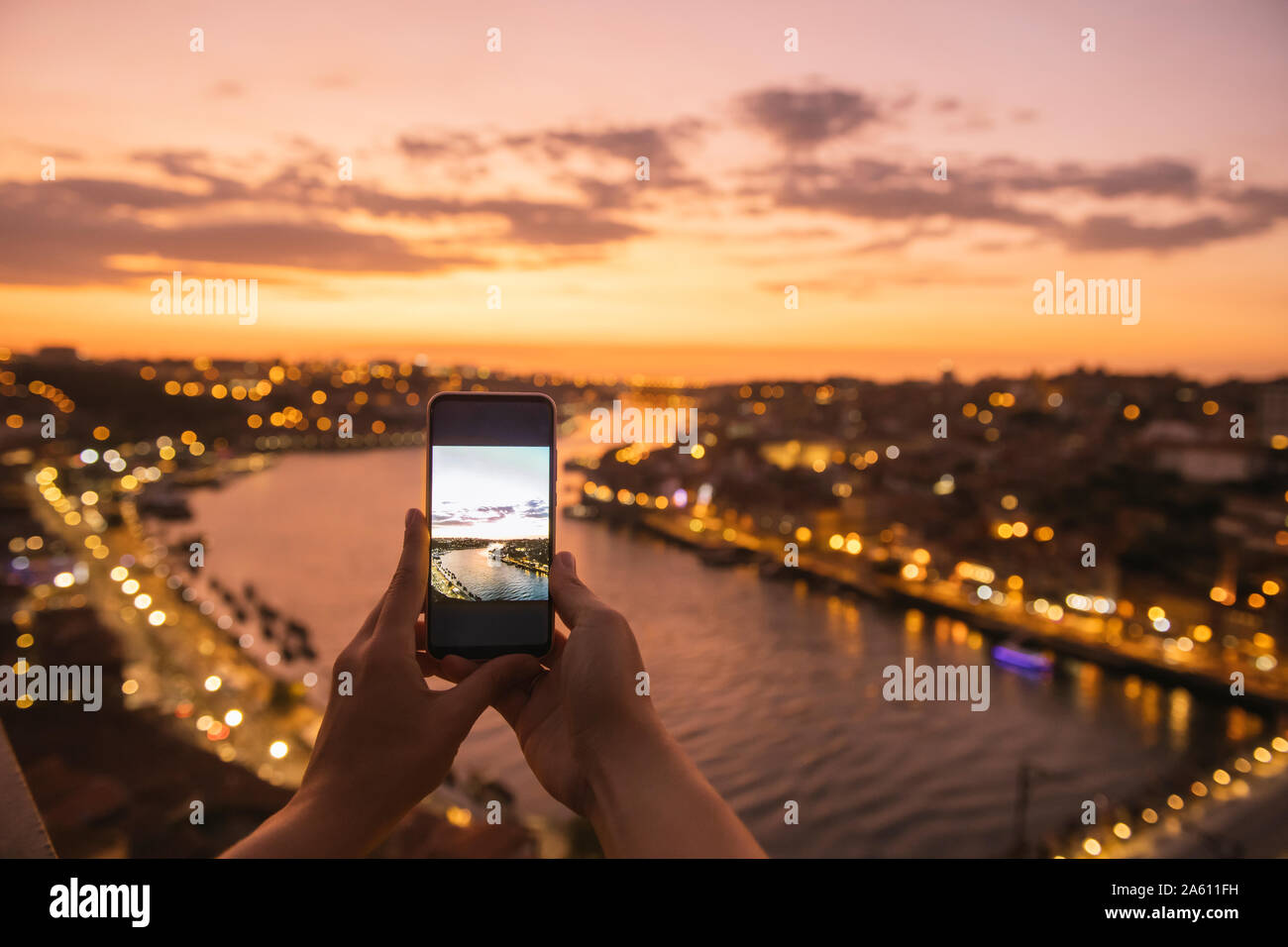 Woman's hands holding smartphone with a photo of panoramic view of Porto at sunset, Portugal Stock Photo