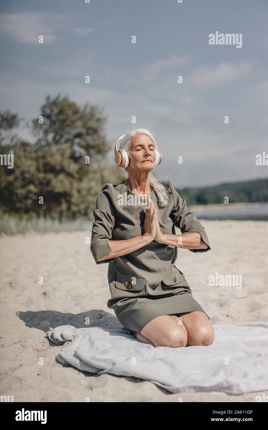 Senior woman meditating with headphones on the beach Stock Photo