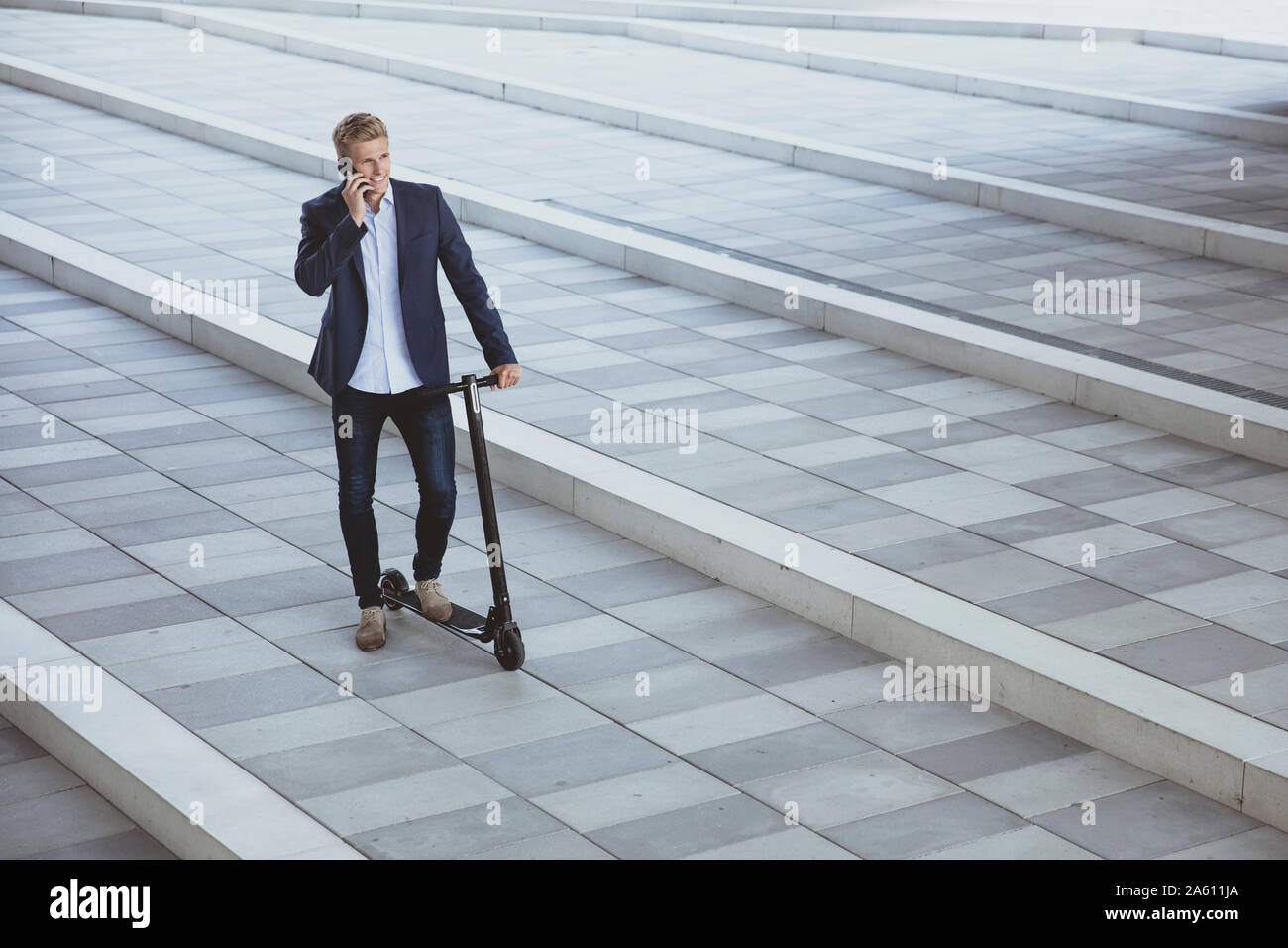 Young man with e-scooter talking on the phone on a city square Stock Photo