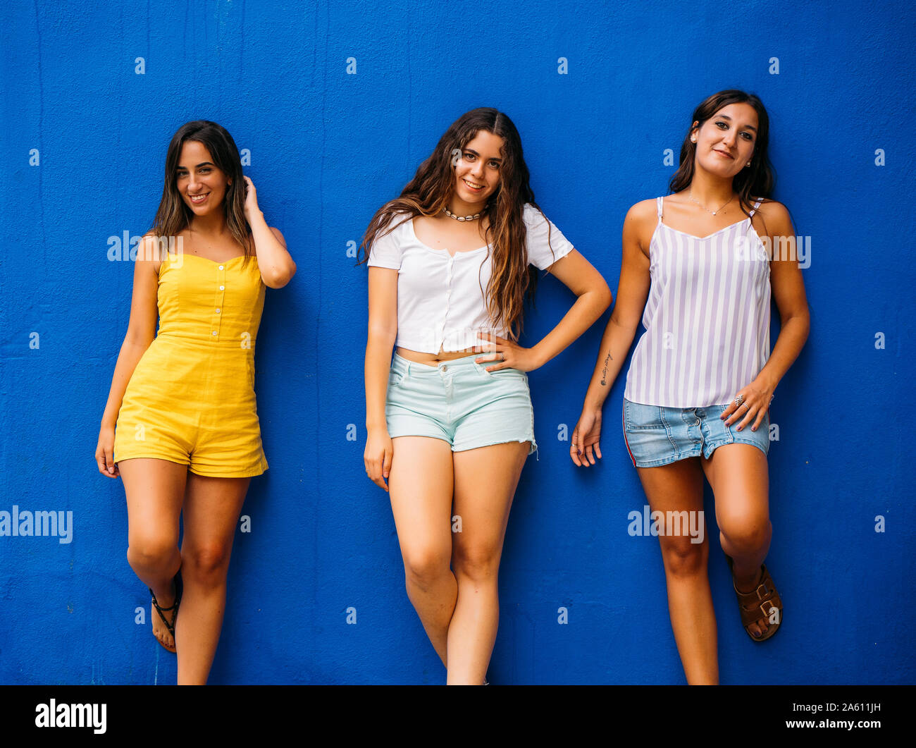 Three beautiful young women posing at a blue wall Stock Photo