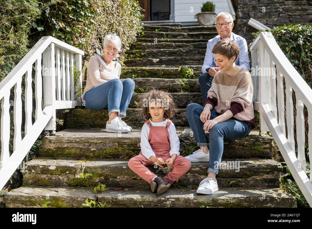 Senior couple with adult daughter and grandson sitting on stairs in garden of their home Stock Photo