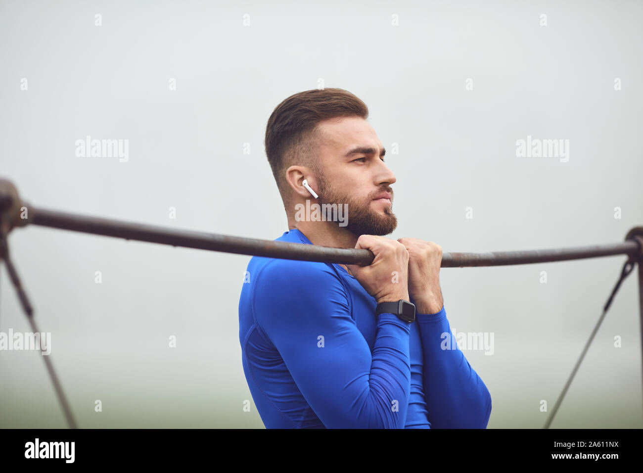 A bearded guy doing pull-ups on a horizontal bar in a stadium in the fog. Stock Photo