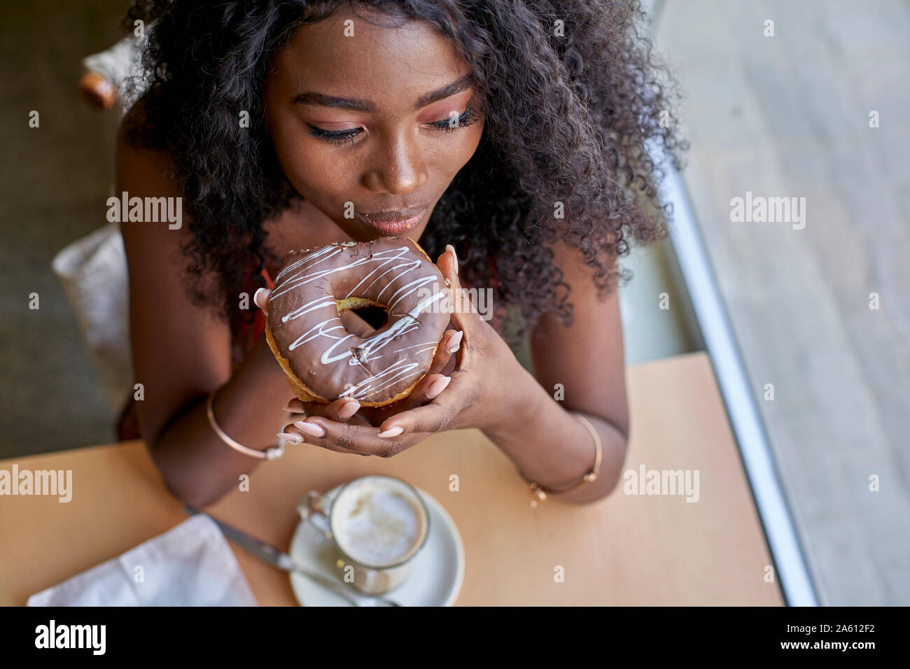 Portrait of young African woman eating a doughnut in a cafe Stock Photo